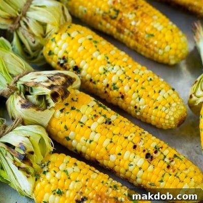 Grilled corn on the cob topped with garlic and herb butter on a sheet pan.