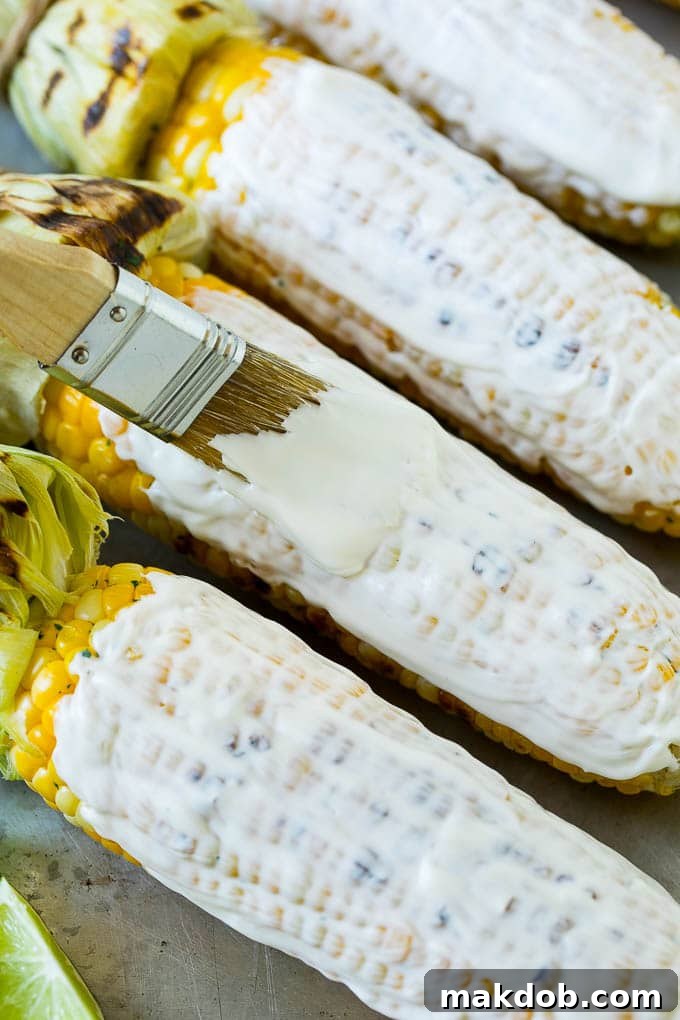 A kitchen brush coating corn on the cob with a creamy mixture of mayonnaise and crema.