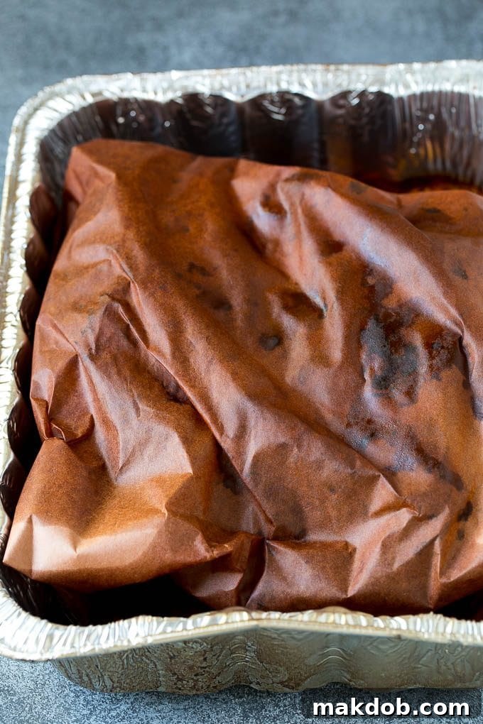 A large beef brisket wrapped securely in peach butcher paper, continuing to smoke for optimal flavor and moisture retention.