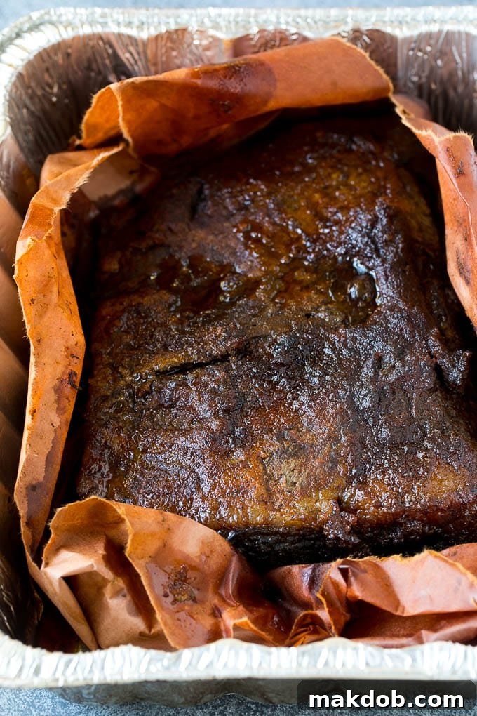 A large piece of beef brisket, perfectly smoked and now wrapped in peach butcher paper, allowing it to tenderize and absorb more smoke.