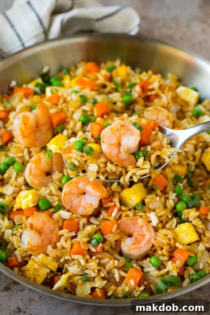 Shrimp Fried Rice Recipe | Chinese Fried Rice #rice #shrimp #peas #carrots #sidedish #dinner #dinneratthezoo A serving spoon in a pan of vibrant shrimp fried rice, showcasing tender shrimp, peas, carrots, and scrambled egg amidst fluffy rice.