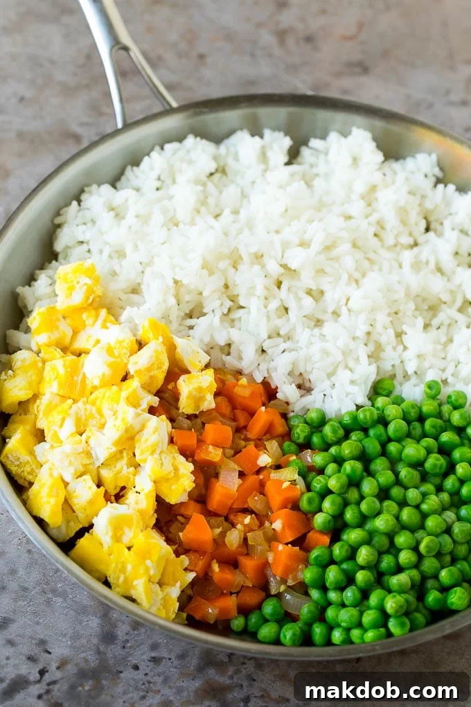 Shrimp Fried Rice Recipe | Chinese Fried Rice #rice #shrimp #peas #carrots #sidedish #dinner #dinneratthezoo A mix of cooked rice, scrambled eggs, bright green peas, and diced carrots in a pan, waiting to be combined for the perfect fried rice.