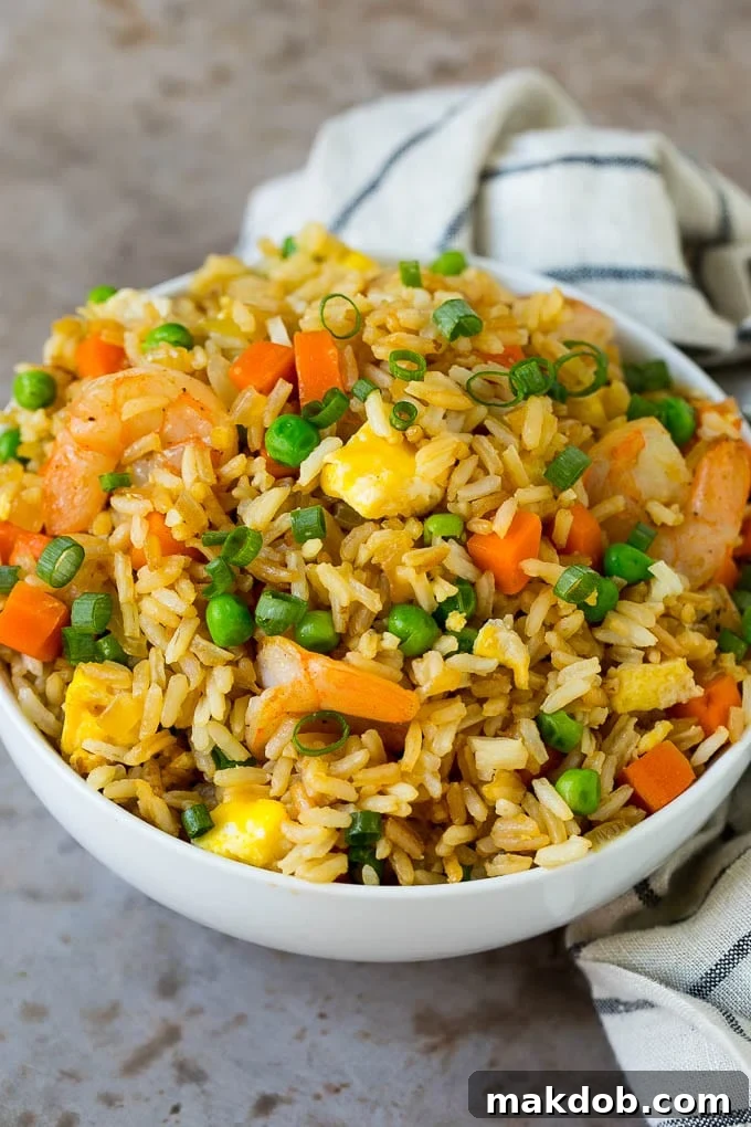 Shrimp Fried Rice Recipe | Chinese Fried Rice #rice #shrimp #peas #carrots #sidedish #dinner #dinneratthezoo A white serving bowl generously filled with homemade shrimp fried rice, garnished with fresh green onions.