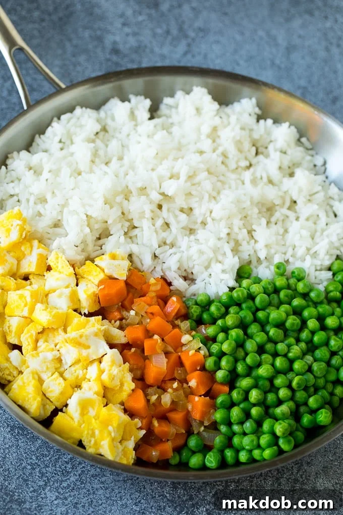 A pan filled with perfectly cooked rice, vibrant carrots, fluffy scrambled eggs, and green peas, ready for the final touches of a delicious fried rice.