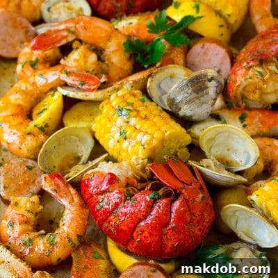 A sheet pan of seafood boil with shrimp, lobster tail, sausage, corn and potatoes.