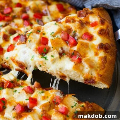 A slice of chicken Alfredo pizza with bacon and fresh tomatoes.