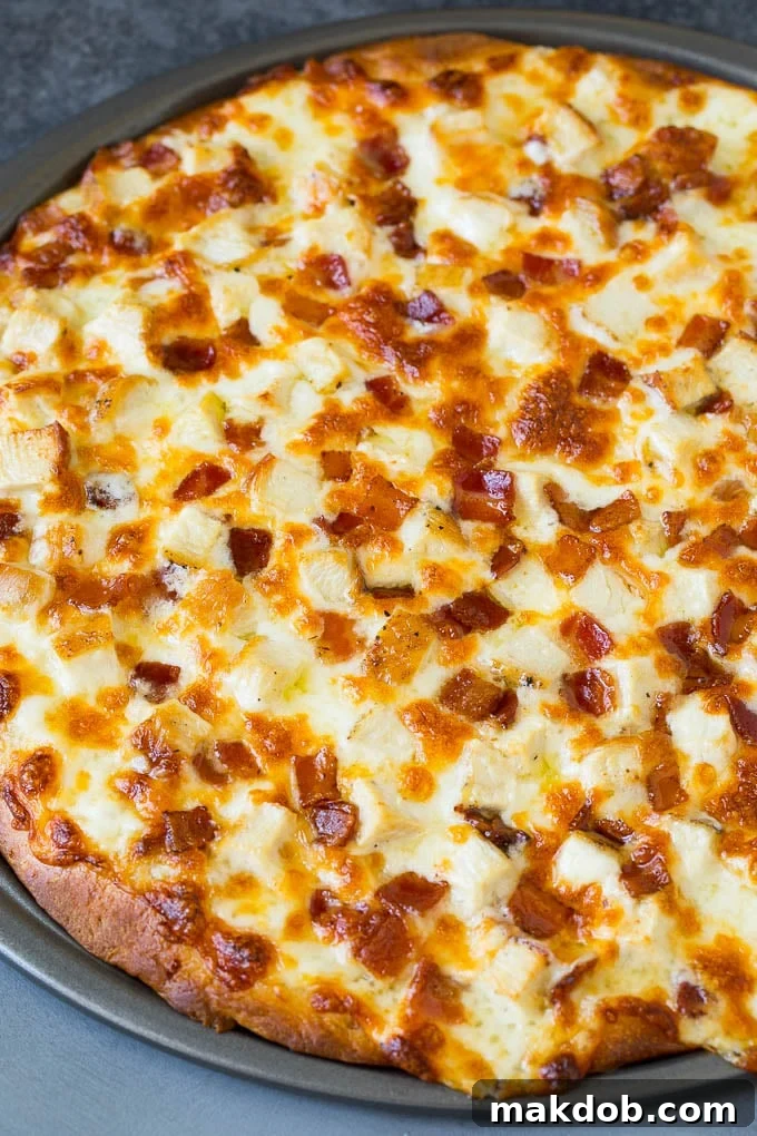 A freshly baked chicken Alfredo pizza with perfectly melted cheese and golden-brown crust, straight out of the oven.