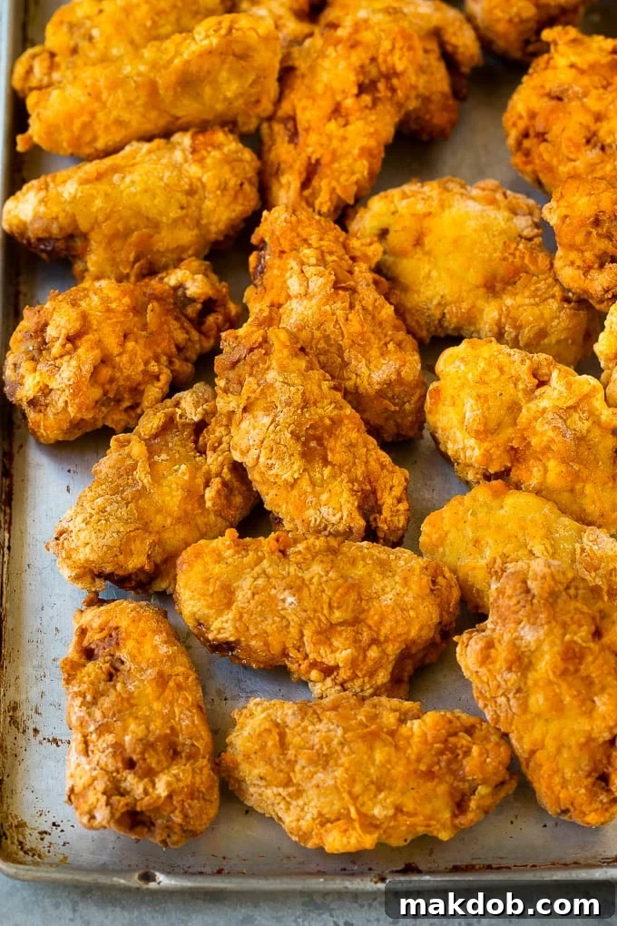 Crispy Fried Wings Draining Freshly deep fried chicken wings draining on a wire rack set over a sheet pan to maintain crispiness.