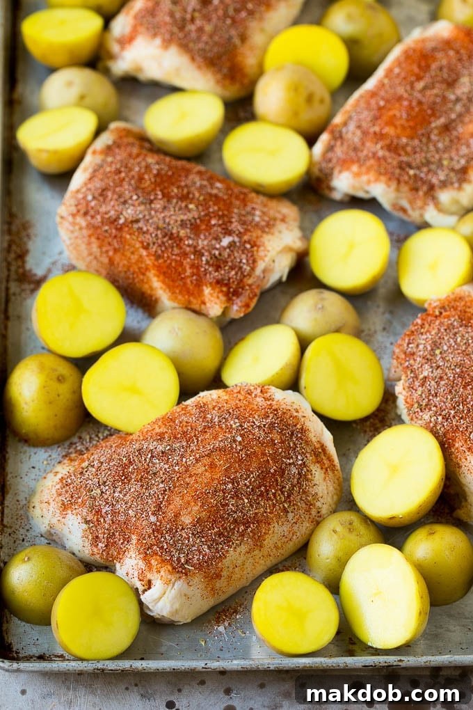Rustic Spanish Chicken and Potatoes 4 Raw chicken thighs coated in a rich spice rub, nestled among small halved Yukon gold potatoes on a sheet pan.