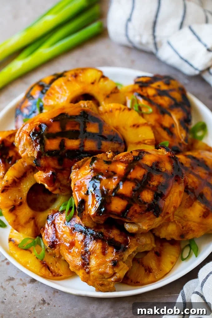 A beautifully plated Huli Huli Chicken dish with perfectly grilled pineapple slices, garnished with fresh green onions, ready to be served. The chicken is caramelized and juicy.