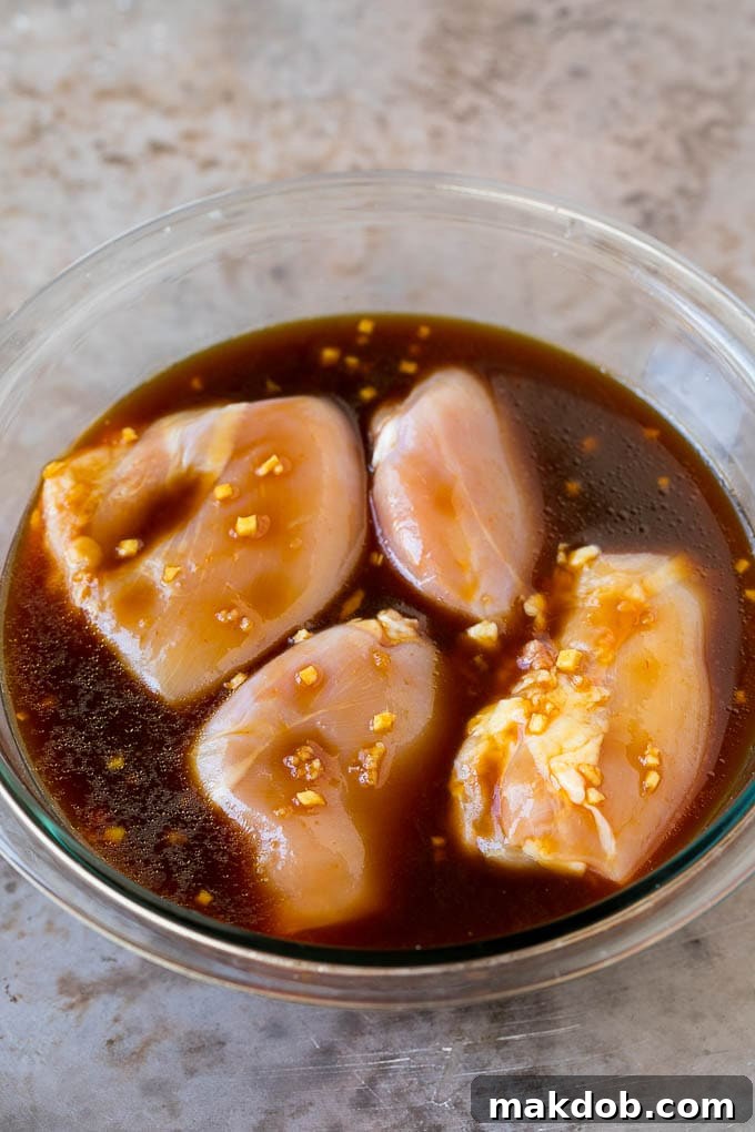 Raw boneless, skinless chicken thighs marinating in a vibrant orange-brown sauce in a glass bowl, ready for grilling.