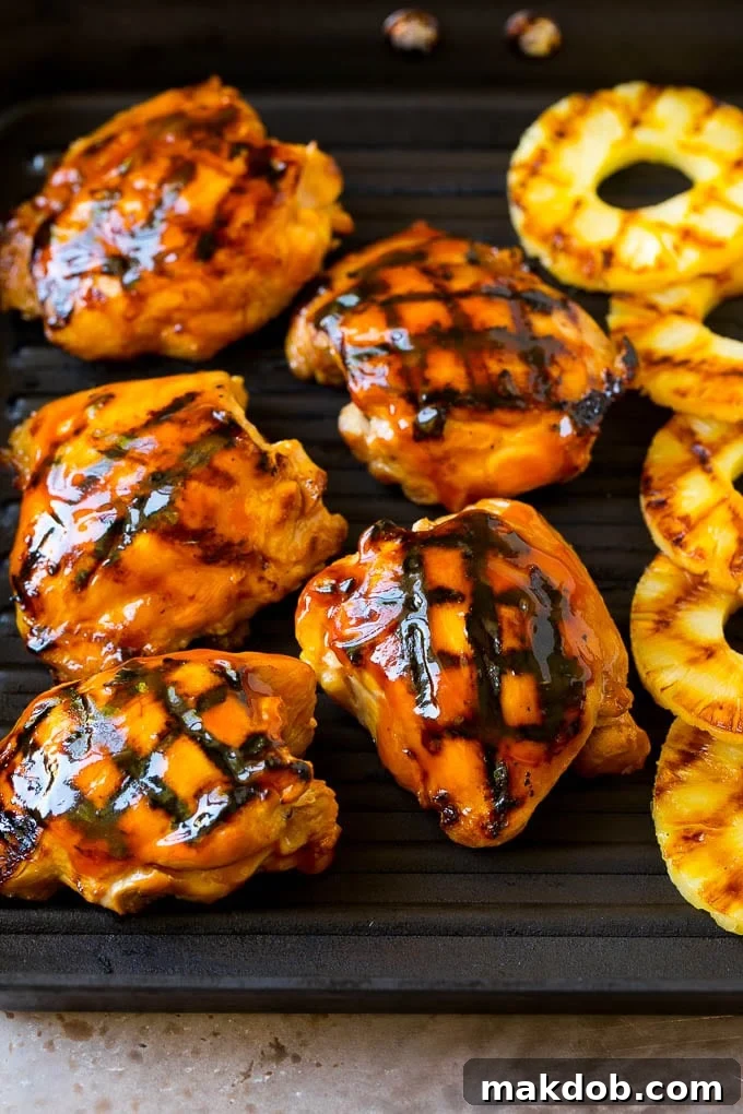 Juicy chicken thighs and fresh pineapple slices sizzling on a hot grill pan, showing delicious char marks.