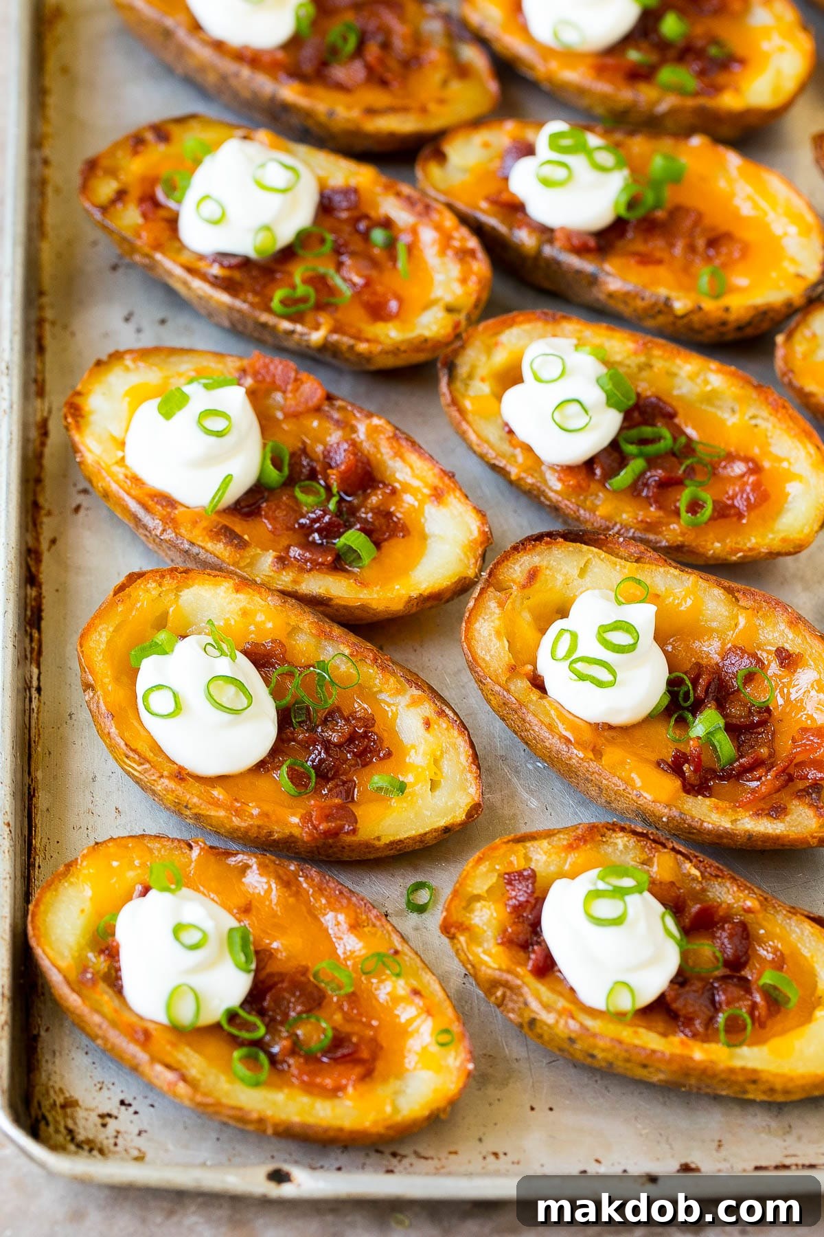 Ultimate Cheesy Bacon Potato Skins 4 A sheet pan filled with golden-brown potato skins, beautifully garnished with fresh sour cream and vibrant green onions, ready for serving.