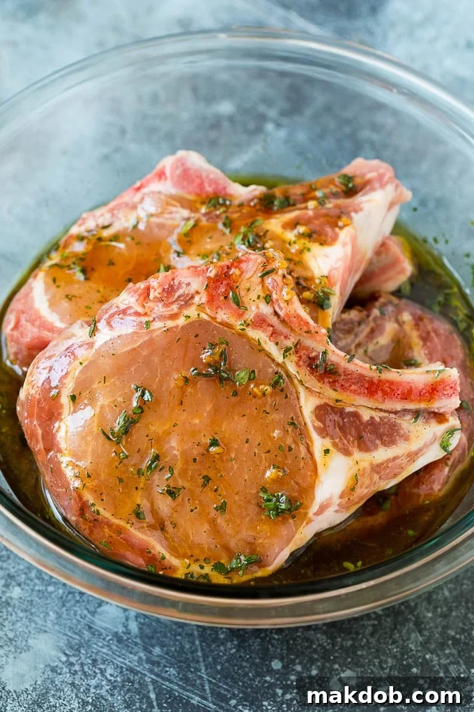 Pork Chops Marinating Pork chops marinating in a flavorful sauce within a glass bowl, ready for the grill.