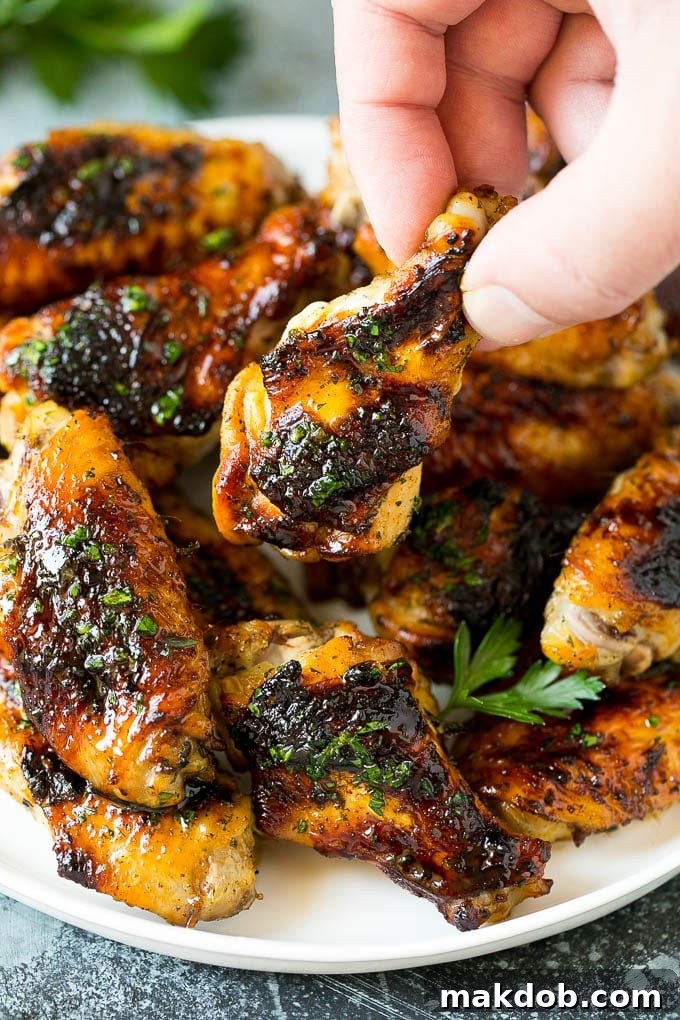 A hand reaching for a grilled chicken wing from a plate.
