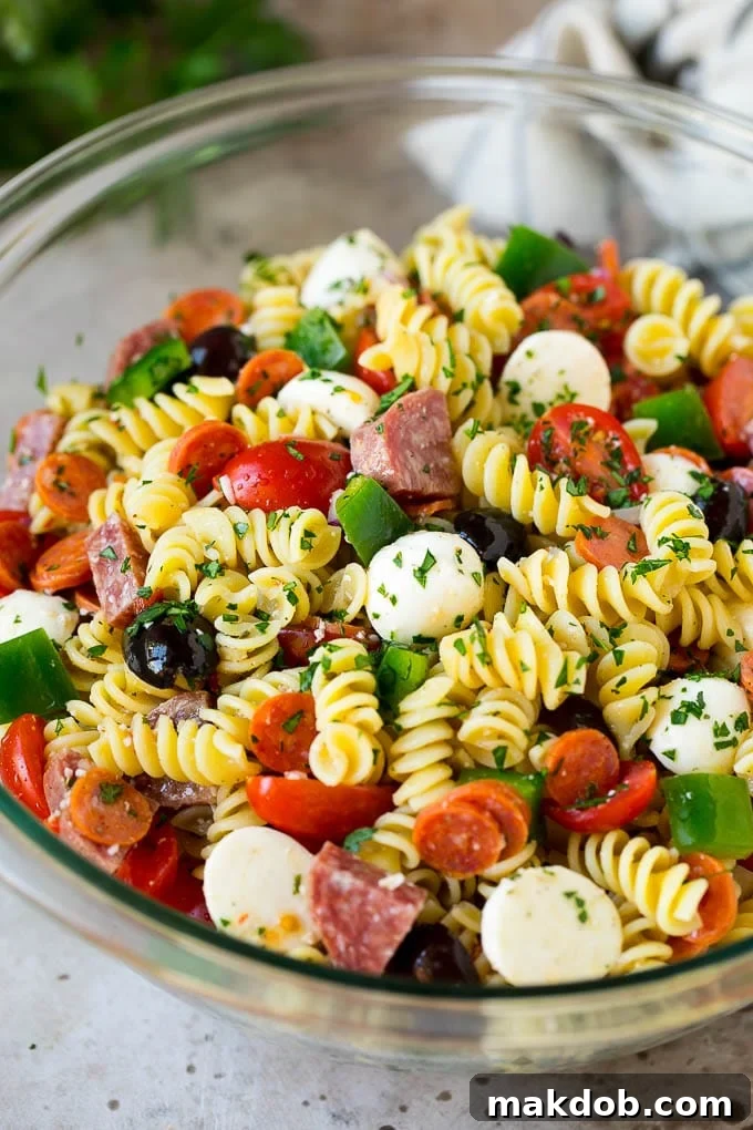 Vibrant Italian pasta salad featuring rotini pasta, sliced salami, and pepperoni, garnished with fresh herbs and a rich, glossy dressing.