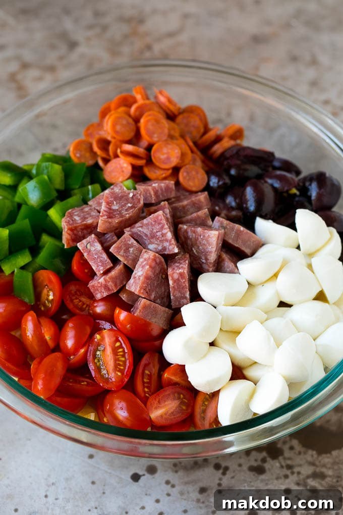 A large bowl filled with a colorful Italian pasta salad, featuring rotini, mozzarella balls, halved cherry tomatoes, vibrant bell peppers, and briny olives, ready to be tossed.