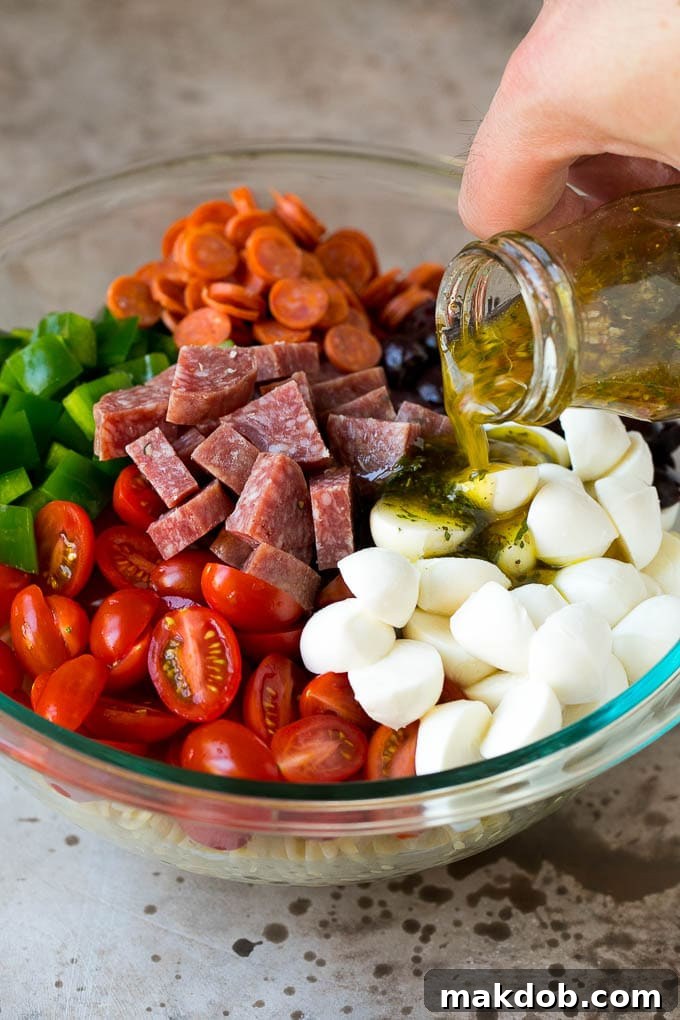 Homemade Italian dressing being drizzled generously over a colorful bowl of pasta salad ingredients, ensuring every component is coated in flavor.