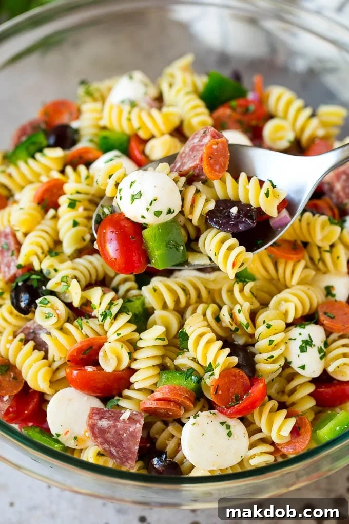 A close-up of a serving spoon scooping a portion of Italian-style pasta salad, showcasing the delightful blend of ingredients and dressing.
