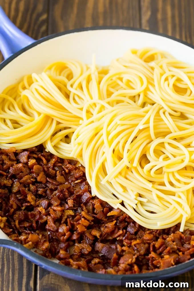 Cooked bacon and spaghetti tossed together in a skillet.