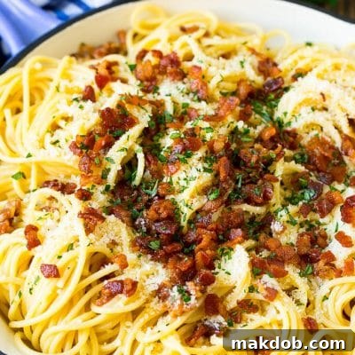 A skillet of pasta carbonara topped with bacon, parmesan cheese and parsley.