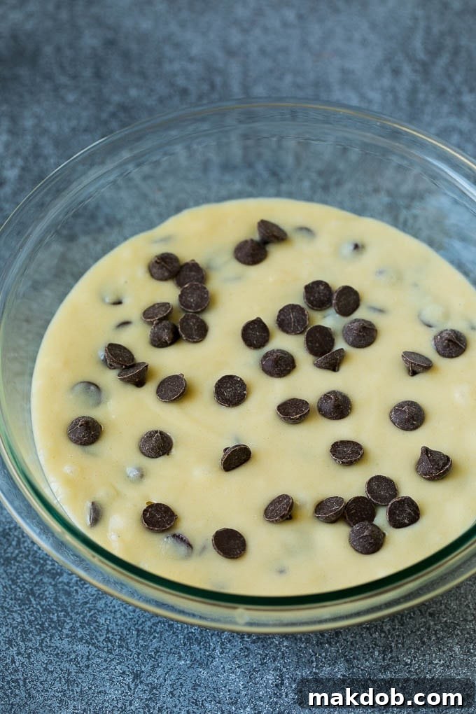 A mixing bowl filled with creamy muffin batter, generously studded with chocolate chips, ready for baking.