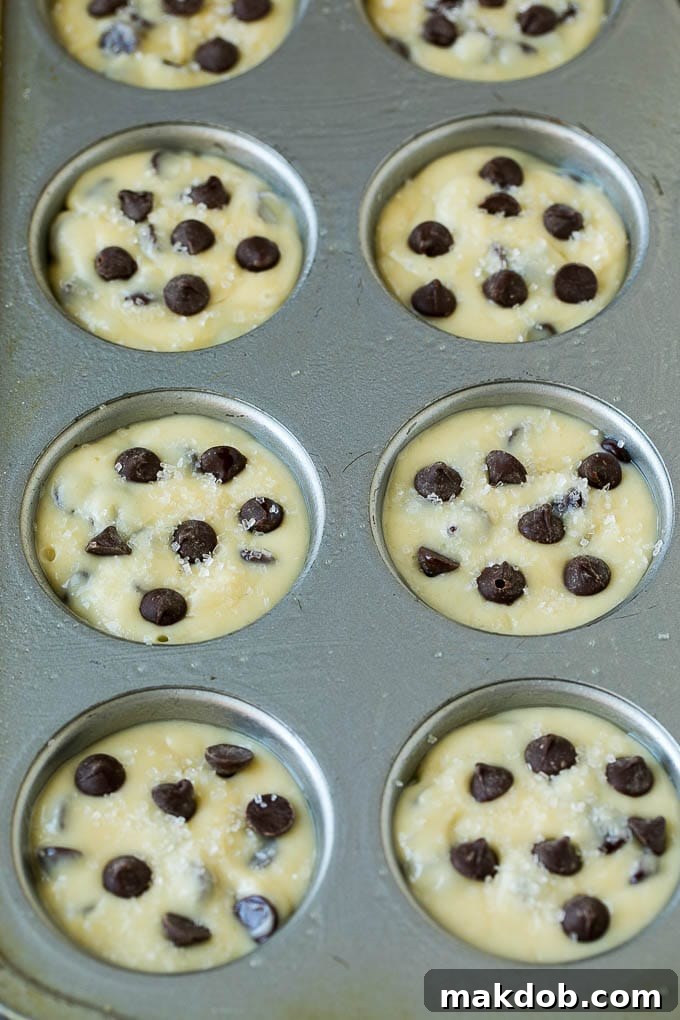 Golden-brown chocolate chip muffins freshly baked and still nestled in their muffin tin, steam gently rising.