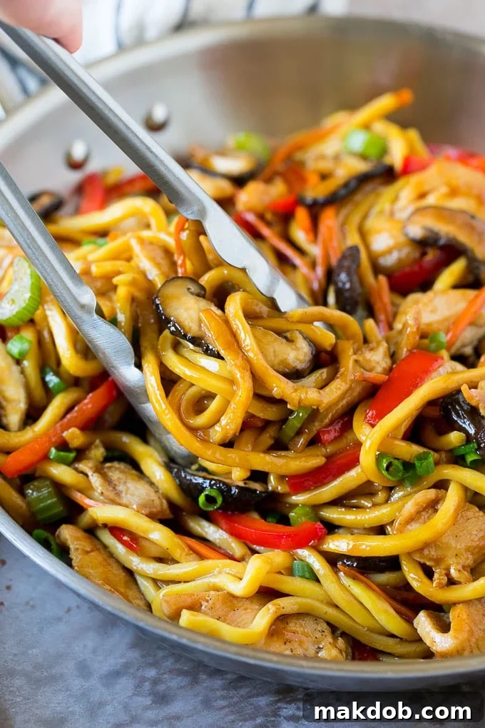 Tongs serving up a portion of chicken and noodle stir fry.