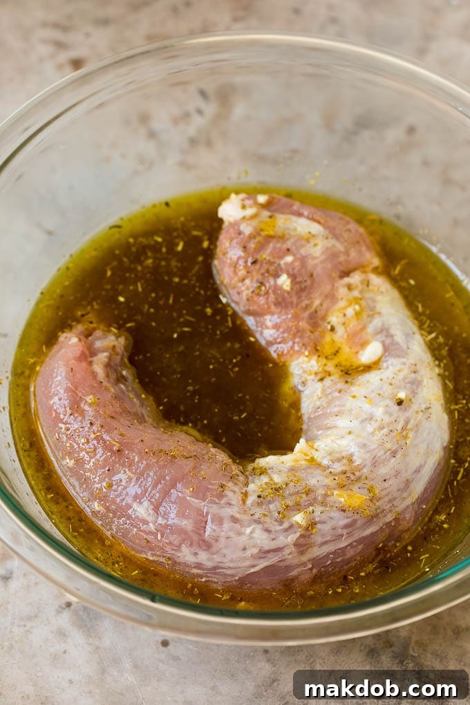 Pork Tenderloin Marinade Pork tenderloin marinating in a citrus and herb blend in a glass bowl, ready to absorb flavors.