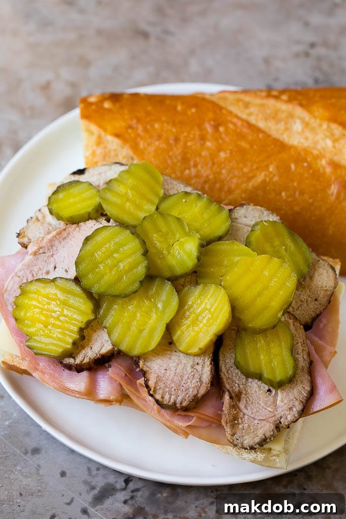 Cuban Sandwich Ingredients Assembled Unassembled Cuban sandwich ingredients: layers of roasted pork, smoked ham, Swiss cheese, and dill pickles laid out on a sliced Cuban bread roll, ready for mustard and topping.