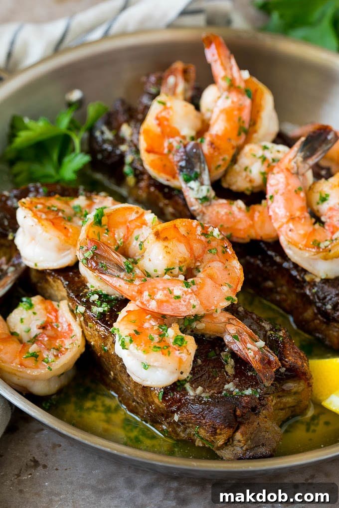 Surf and turf with seared strip steaks topped with jumbo shrimp in garlic butter, garnished with fresh parsley.