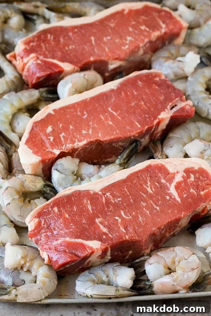 Raw steaks and shrimp on a sheet pan, ready for cooking.