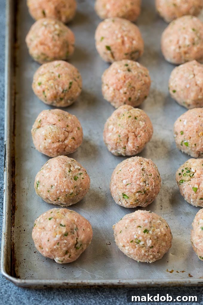 Raw, perfectly shaped turkey meatballs arranged on a baking sheet, ready for broiling.