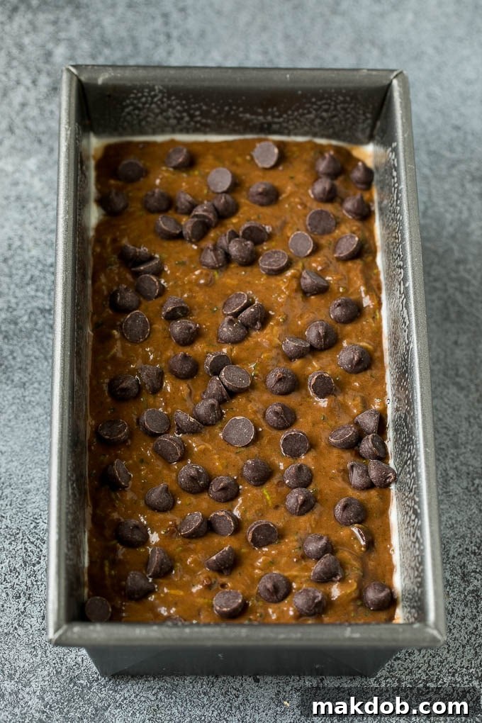 Zucchini bread batter being poured into a greased loaf pan, ready for baking.