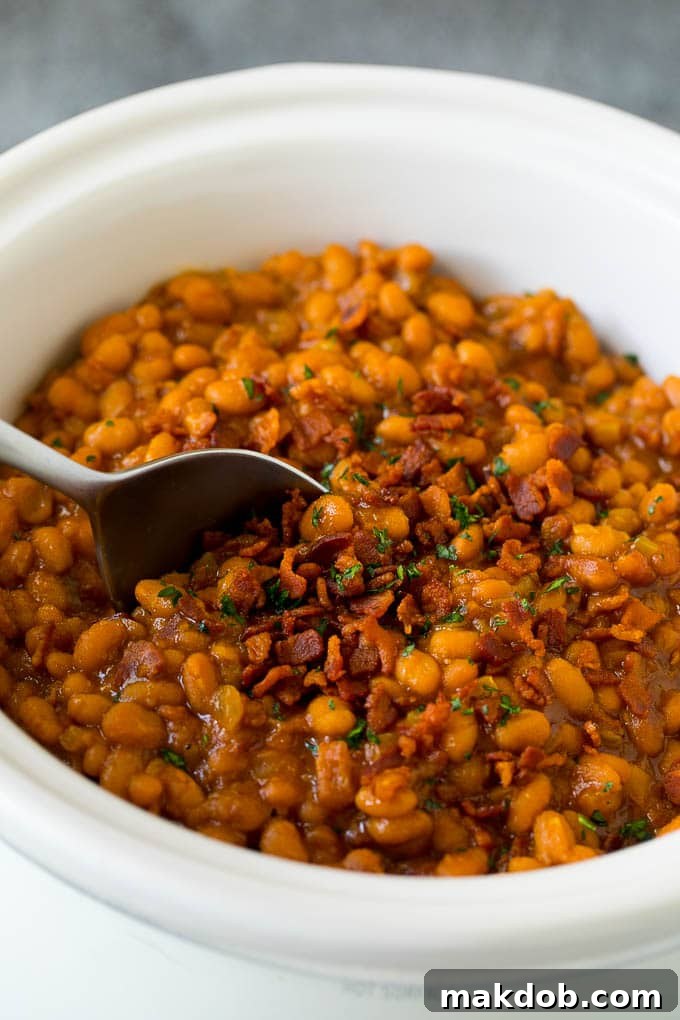 Crock Pot Baked Beans | Slow Cooker Baked Beans #beans #bacon #slowcooker #crockpot #dinneratthezoo Crock pot baked beans with bacon, with a serving spoon in the pot.