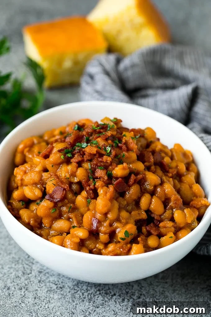 Crock Pot Baked Beans | Slow Cooker Baked Beans #beans #bacon #slowcooker #crockpot #dinneratthezoo A bowl of crock pot baked beans topped with crispy bacon and served with cornbread.