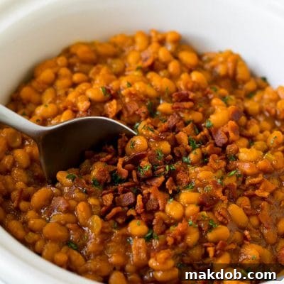 Slow Cooker Sweet & Smoky Baked Beans 2 Crock pot baked beans with bacon, with a serving spoon in the pot.
