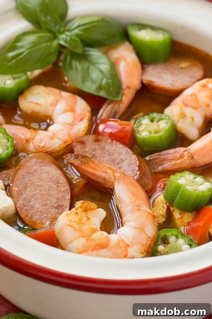 Single Skillet Surf & Turf Gumbo 6 A spoonful of One Pot Chicken and Shrimp Gumbo being lifted from the pot, showing the rich broth and various ingredients, emphasizing its easy 30-minute preparation.