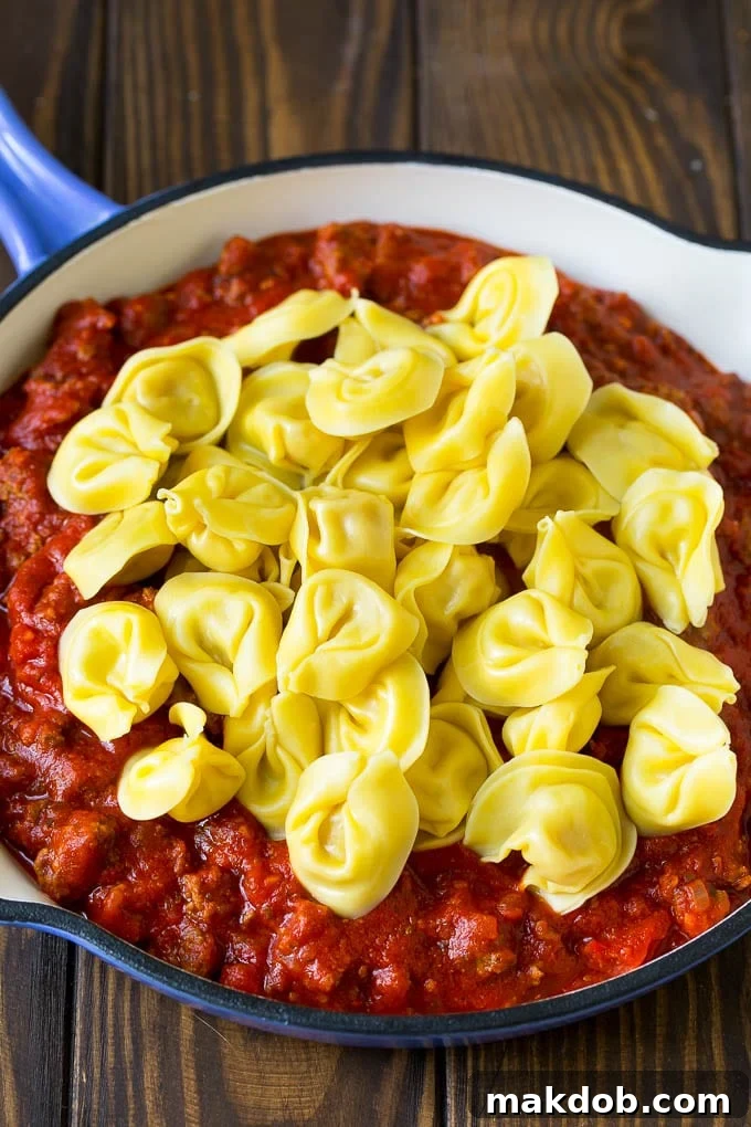 Cooked tortellini over meat sauce in a skillet.