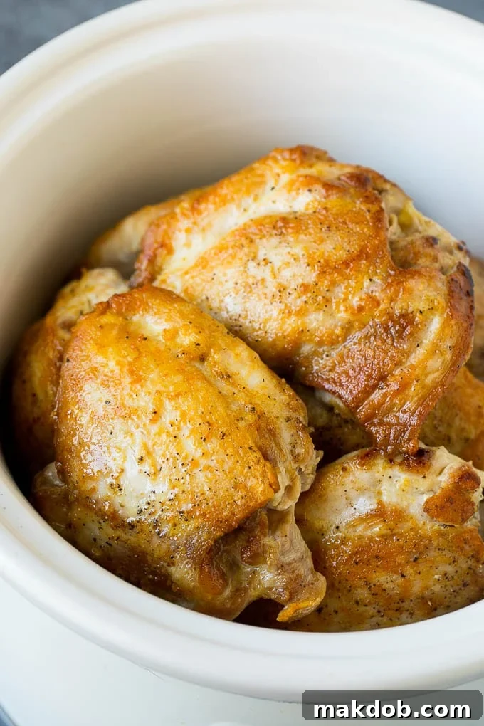 Golden-brown, seared chicken thighs arranged neatly within the ceramic insert of a crock pot, ready for slow cooking.