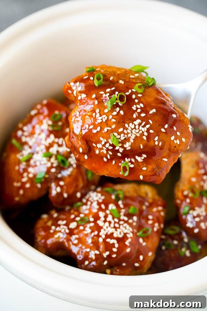 A serving spoon lifting a portion of tender honey garlic chicken from the slow cooker, highlighting the rich sauce.