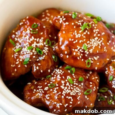 Slow cooker chicken thighs garnished with sesame seeds and green onions, beautifully plated.