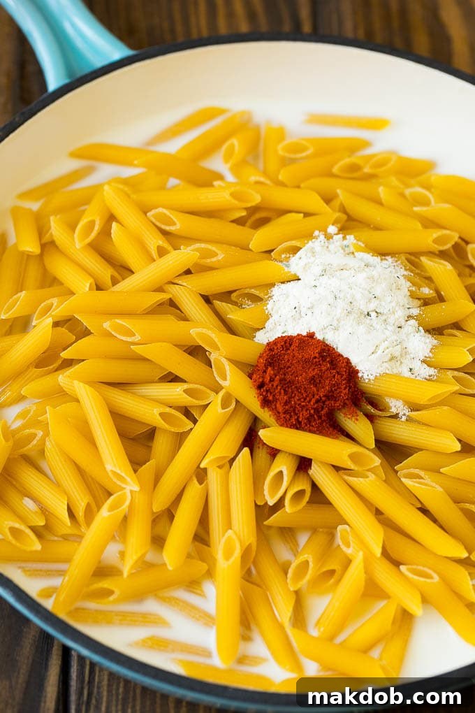Penne pasta with seasonings simmering in a pan of milk and water.