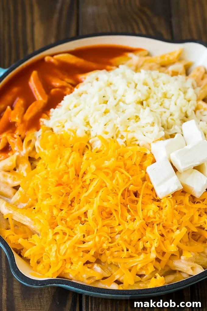 Cooked penne pasta topped with three cheeses and buffalo sauce, before baking.
