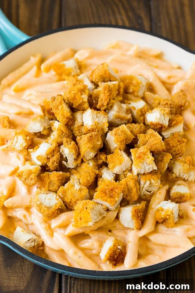 Chopped chicken tenders scattered on top of cheesy pasta, before the final bake.