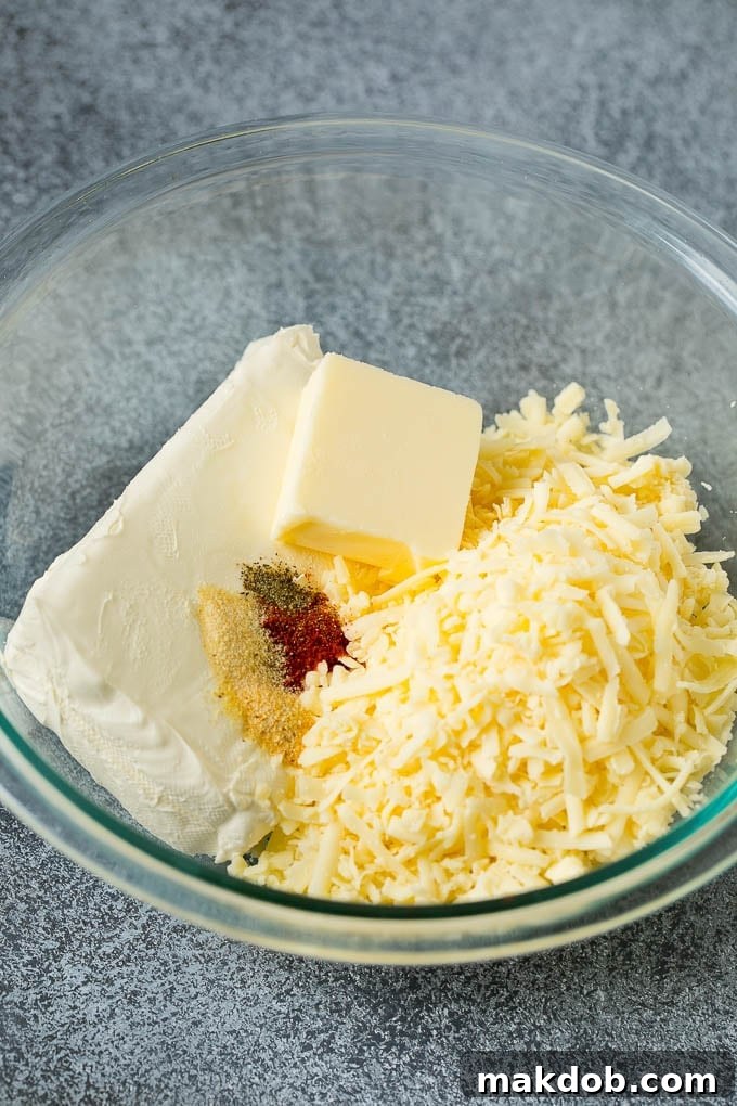 Irresistible Cheese Ball Appetizer 3 Shredded cheese, cream cheese, butter and spices in a mixing bowl.
