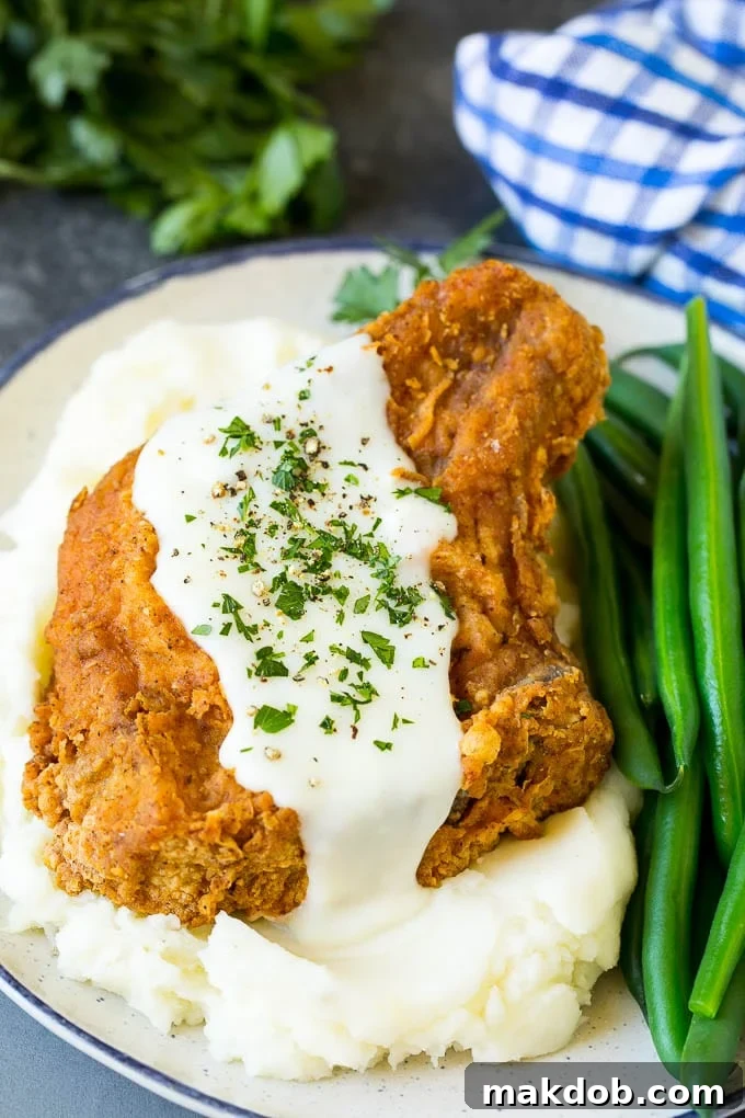 A fried pork chop served over mashed potatoes with green beans.