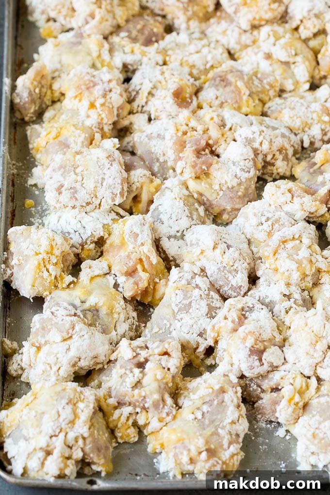 Cubed chicken pieces coated in a dry batter of flour and cornstarch, ready for frying.