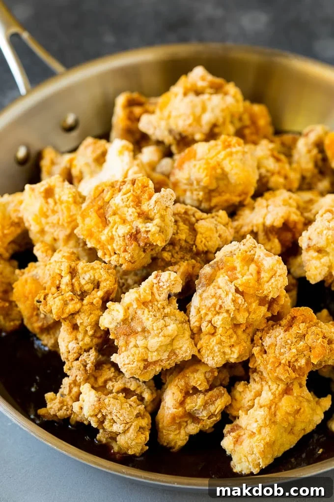 Crispy General Tso's chicken simmering in a rich, spicy, and sweet sauce in a skillet.