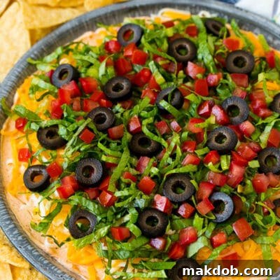 Taco dip with layers of seasoned cream cheese, lettuce, tomato, shredded cheese and olives.